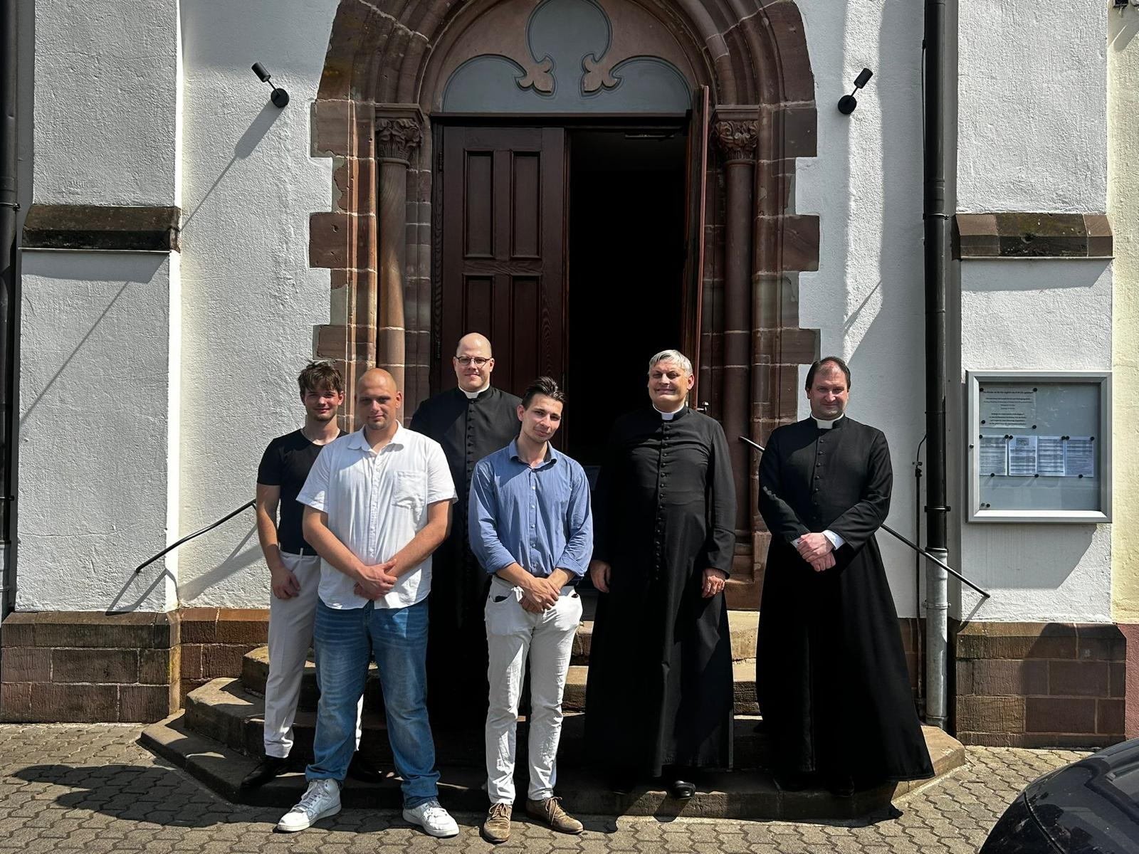Junge Männer mit Priestern vor dem Kirchenportal
