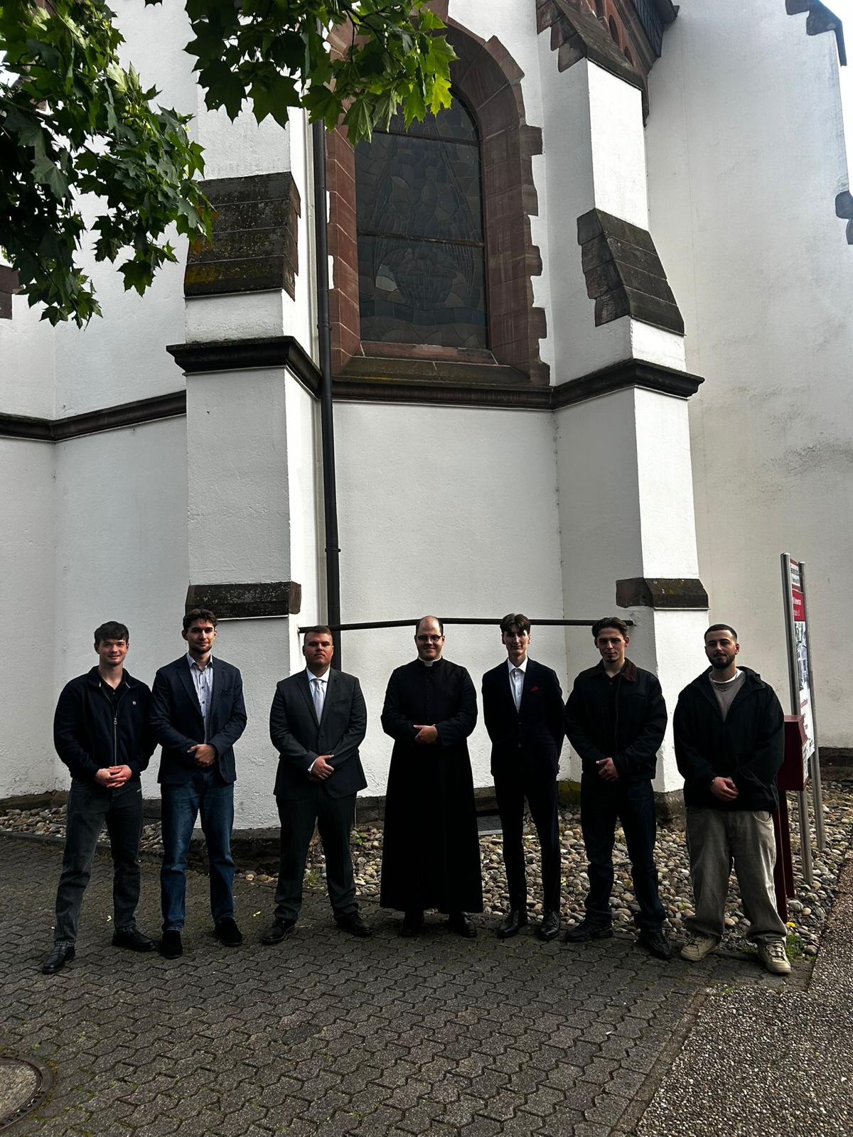Gruppe junger Katholiken mit Priester vor der Kirche
